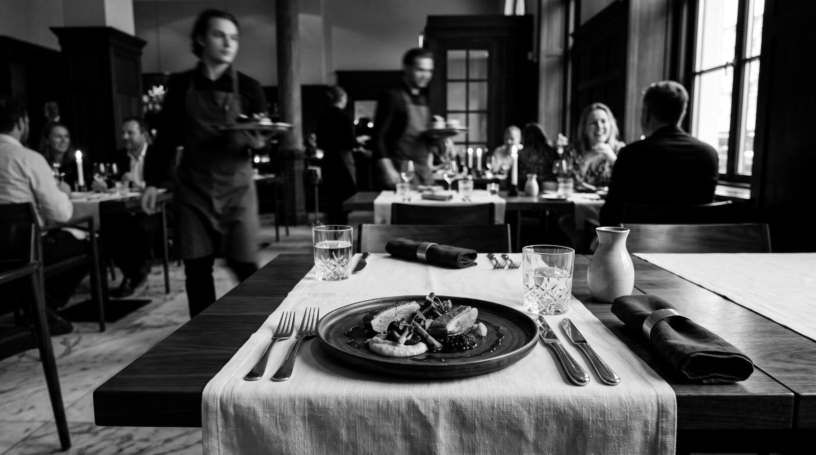 Finished haute-cuisine plate, razor sharp; dining room dissolving into warm bokeh behind